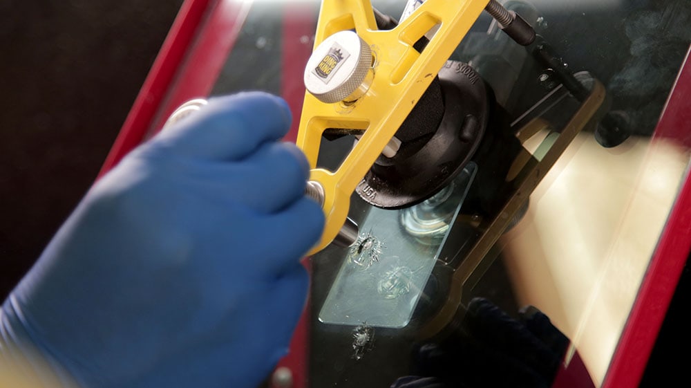 A person in blue gloves is holding a yellow tool during windshield repair training.