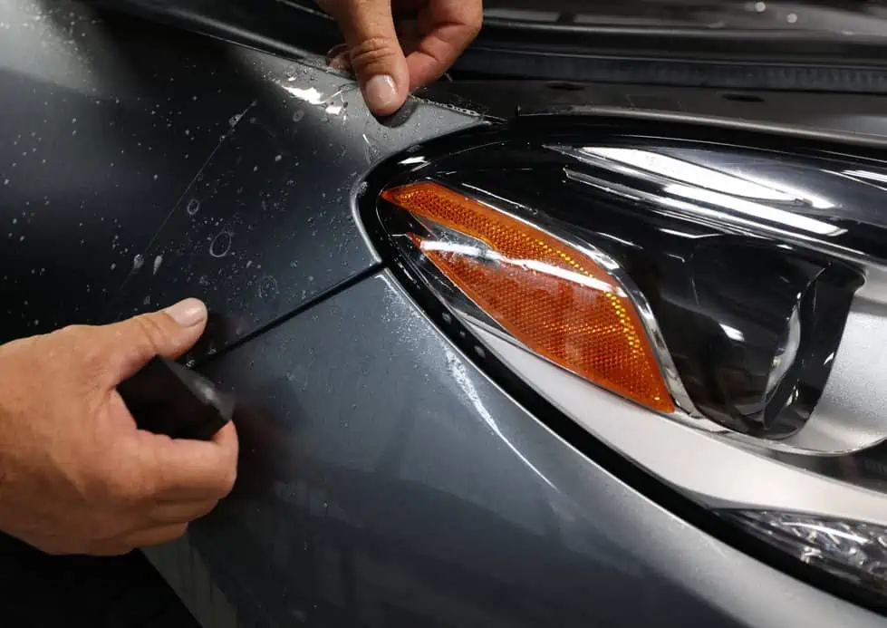 A person is training to apply paint protection film on the headlight of a car.