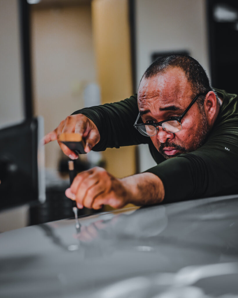 A man receiving paintless dent repair training while working on a car.