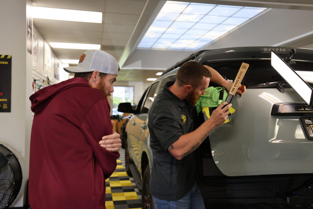 Instructor showing a student how to tap out a dent with a dent hammer using a dent light.