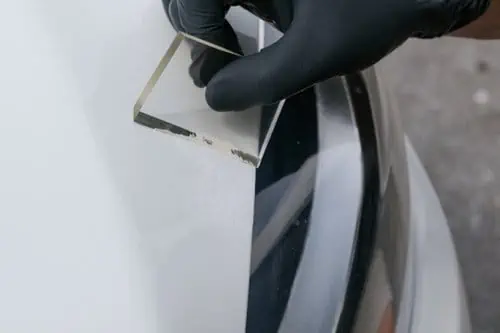 A person in black gloves is performing paint chip repair on a car.