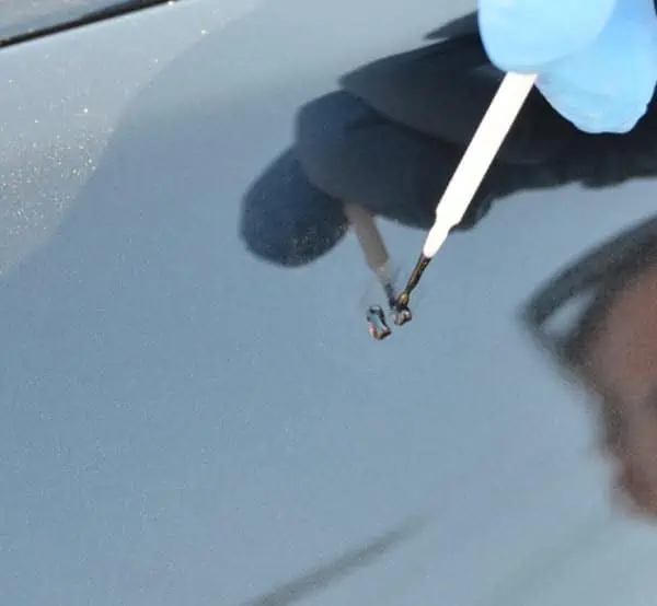 A person is performing paint chip repair on the hood of a car during training.
