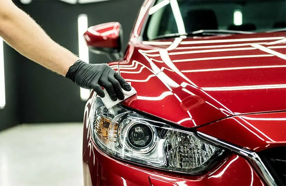 A person is polishing and applying ceramic coating to the hood of a red car.