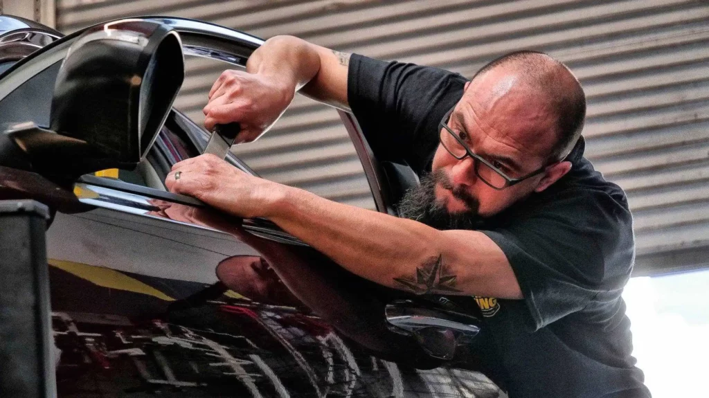 A PDR Technician with a beard is working on a car.