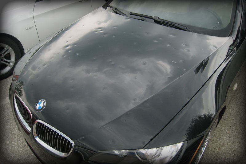 A black car hood under a cloudy sky after hail damage, prompting the need for hail repair training.