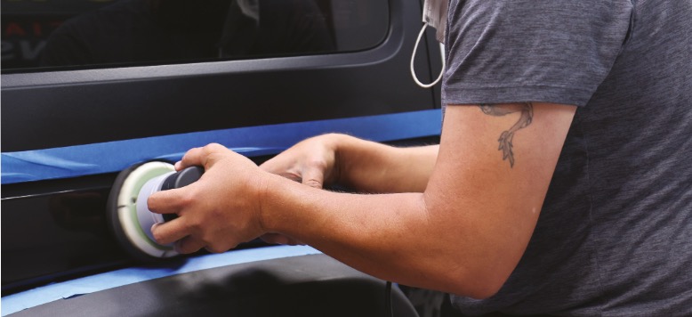 A man is using a tool for paint correction training on the side of a car.