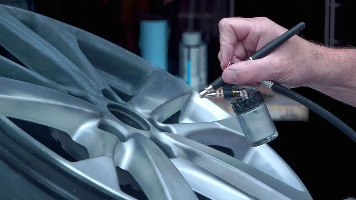 A man is training in alloy wheel repair, spraying a rim with an air brush.