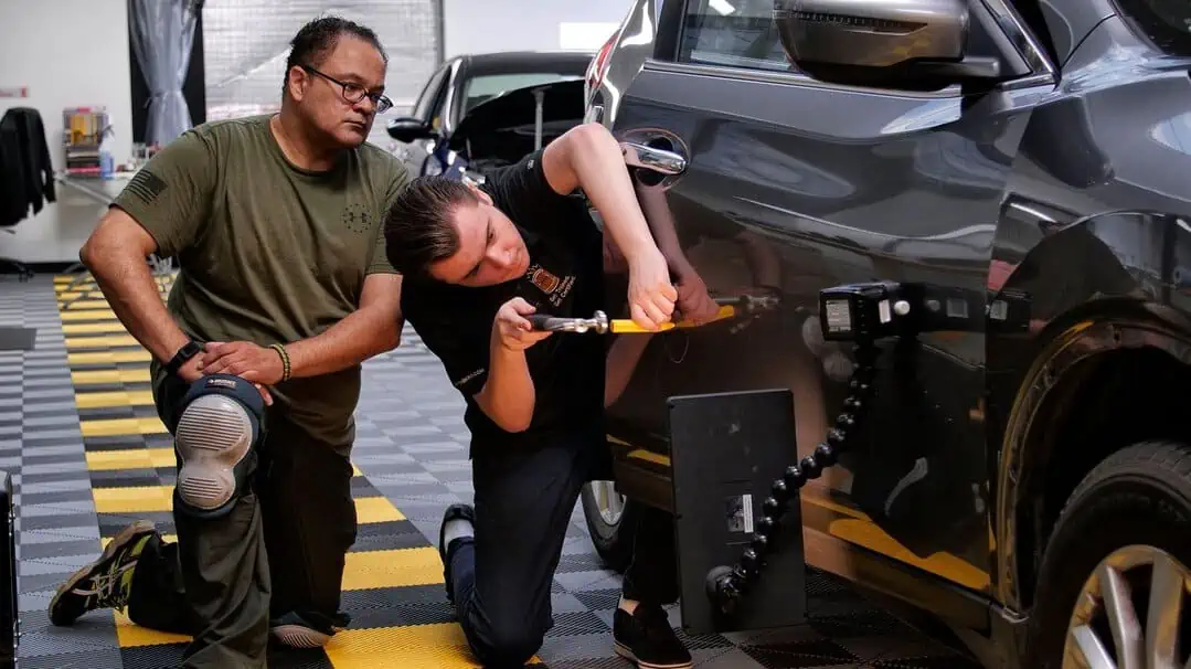Two men honing their paintless dent repair skills in a garage.