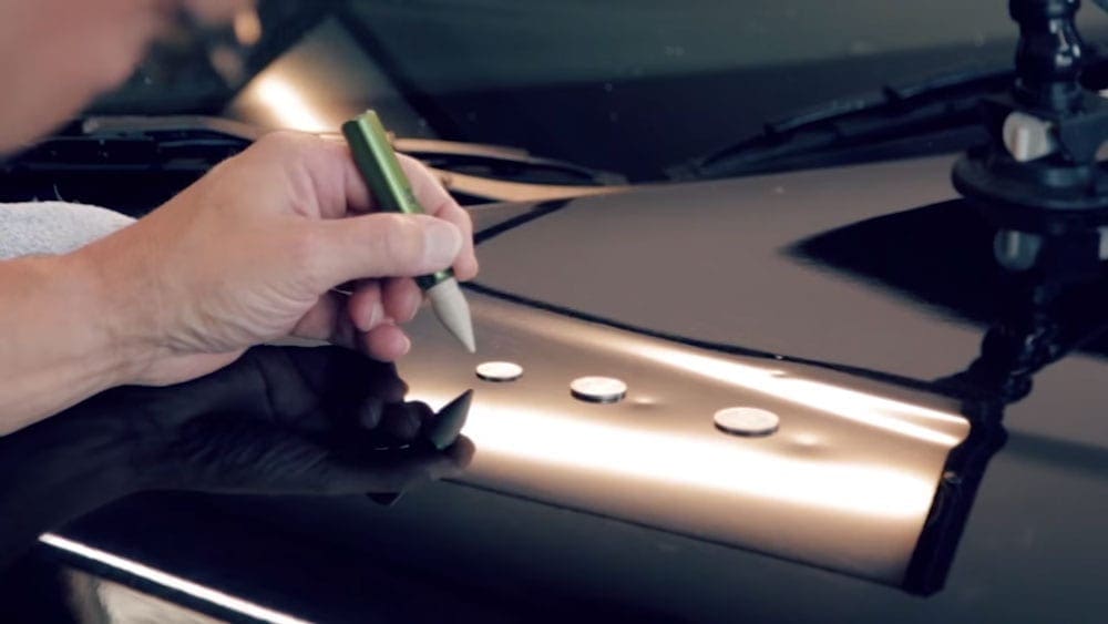 A man is using a marker to identify dents on a car.