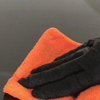 A hand in a black glove carefully wiping an orange towel during paint chip repair training.