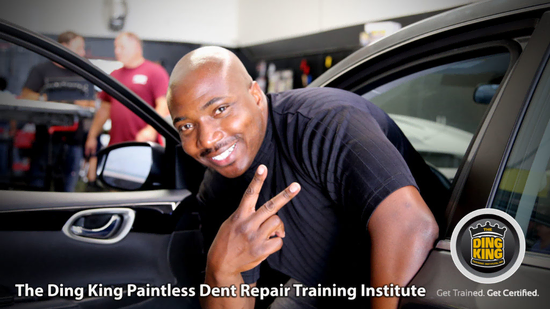 A man smiles while making a peace sign beside an open car door at The Ding King Paintless Dent Repair Training Institute. Text reads, "The Ding King Paintless Dent Repair and Hail Repair Training Institute. Get Trained. Get Certified.