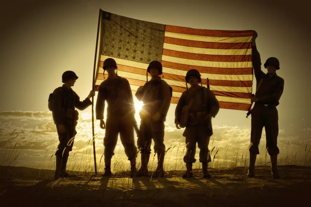 Five soldiers stand together, silhouetted against the bright light of a sunset, holding an American flag. Their unity embodies the same dedication found in hail repair training, where precision and teamwork are key.