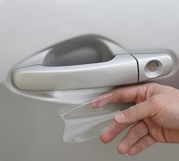 A hand is placing a clear protective film underneath a car door handle to prevent scratches, showcasing techniques learned in paint protection film training.