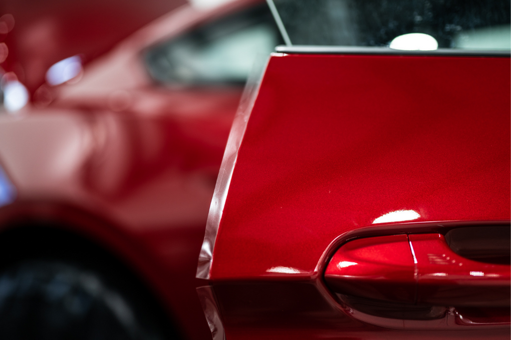 Close-up of a red car's rear side, focusing on the top edge and part of the rear light. The vehicle's sleek and shiny paint, likely benefiting from Paint Protection Film Training, is evident.