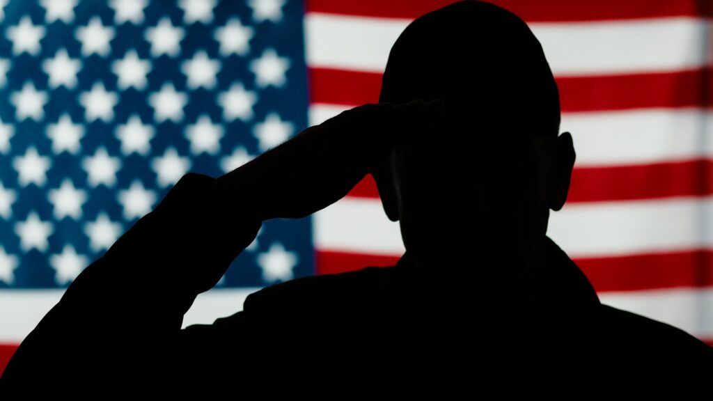 Silhouette of a person saluting with an American flag in the background, captured during a Ceramic Coating Training event.