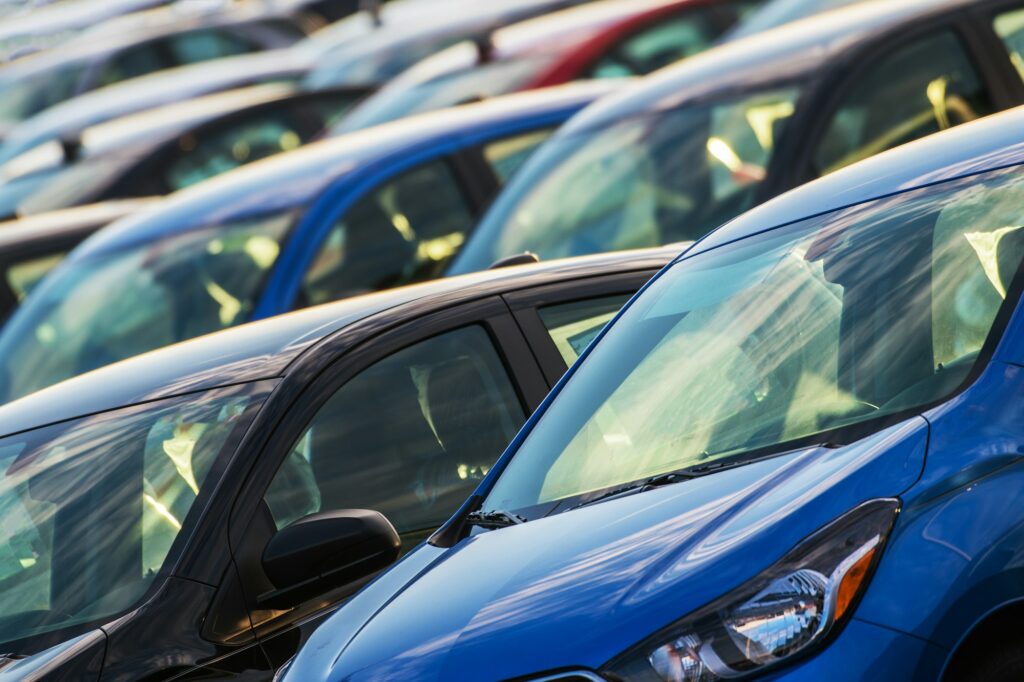 Rows of parked cars in a lot, showcasing a variety of colors including blue, black, and red. Among them are vehicles treated in Ceramic Coating Training sessions, gleaming under the sunlight with an impressive finish.