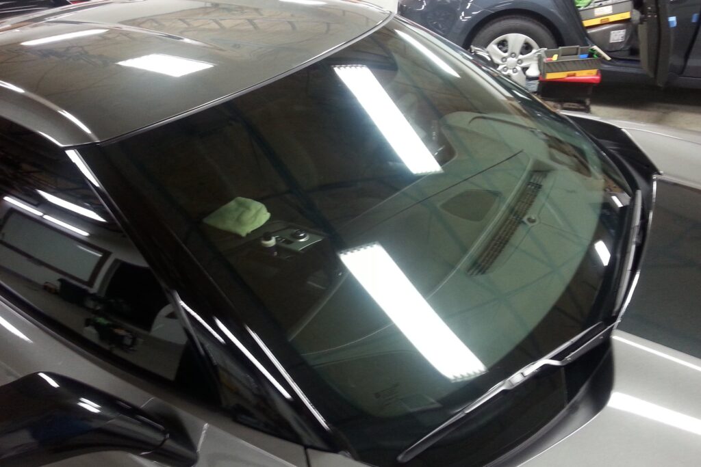 A reflective car windshield with bright overhead lights and a cloth resting on the dashboard, taken from outside the vehicle during Paint Protection Film Training.