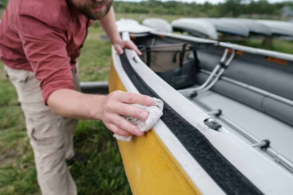 A person in a red shirt cleans the edge of a yellow canoe with a cloth, demonstrating skills akin to Paint Protection Film Training.