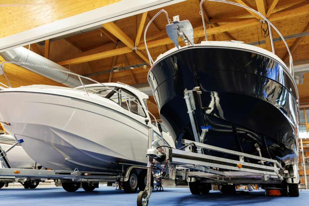 Two motorboats on trailers are displayed indoors, parked side by side on a blue carpet. The boats, situated under a wooden ceiling with exposed beams, look pristine and well-maintained—ideal subjects for Paint Protection Film Training sessions.