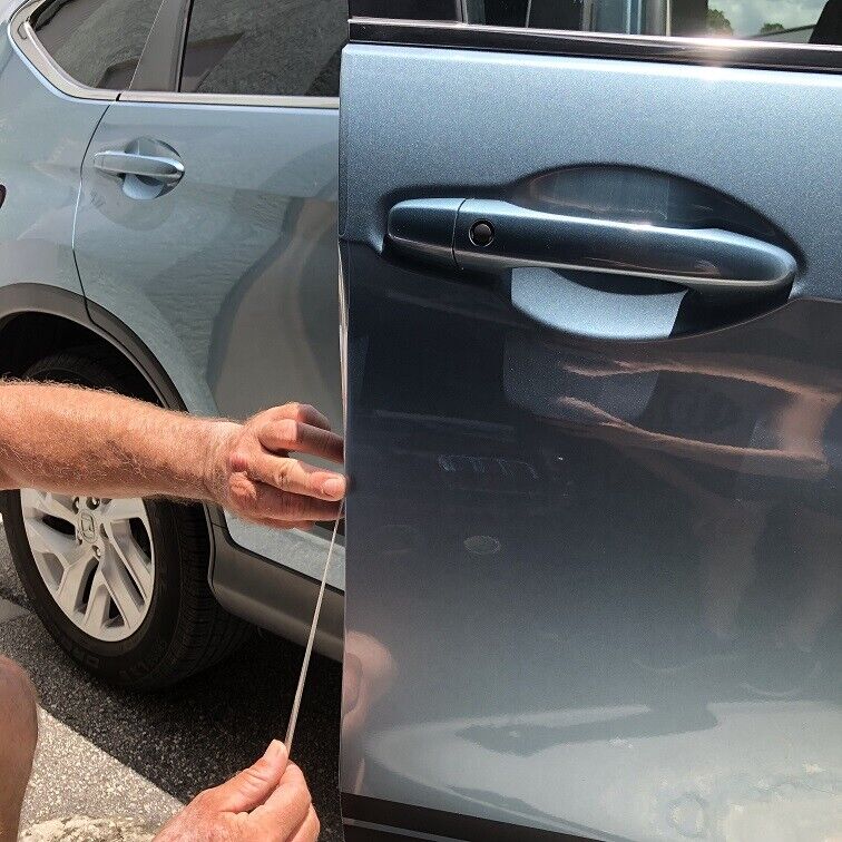 A person is applying a protective film to the edge of a car door to prevent scratches, expertly using a squeegee tool to smooth it out—a skill honed through paint protection film training.