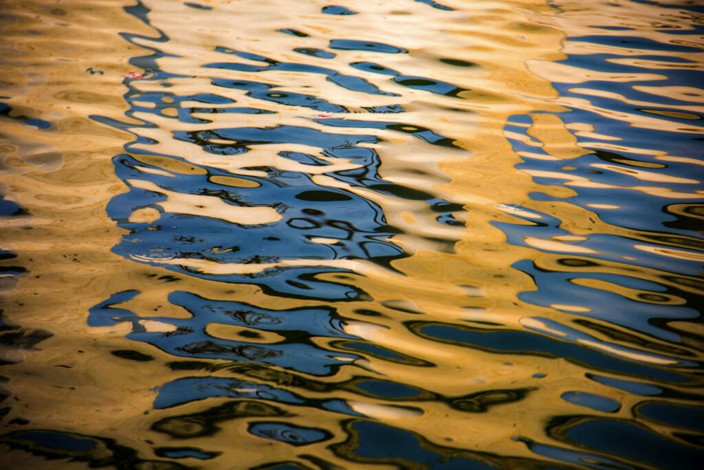 Rippling water reflecting a mix of golden and dark hues, creating an abstract pattern reminiscent of the precision seen in Paint Protection Film Training.