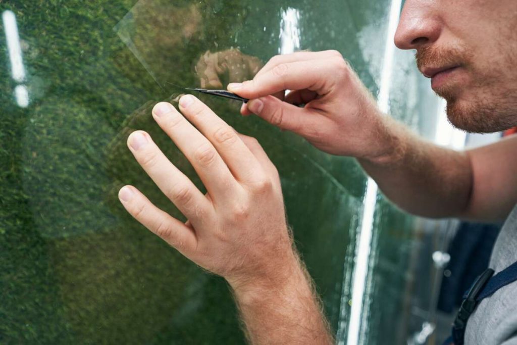 A person meticulously peels the protective film from a glass sheet, demonstrating techniques akin to those learned in Paint Protection Film Training.