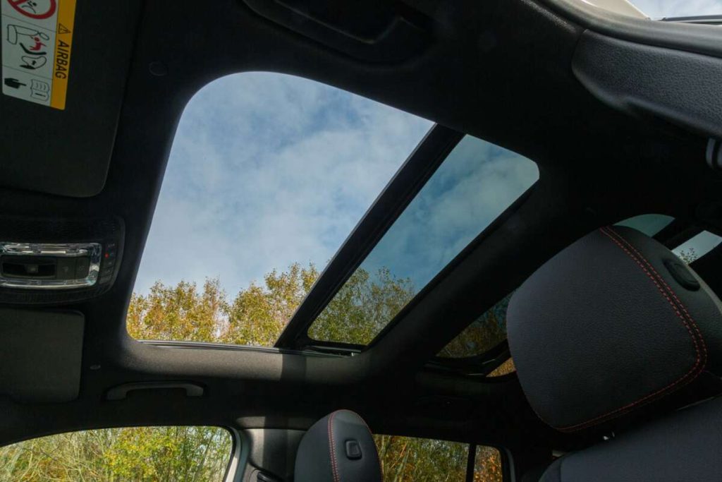 View from inside a car showing a panoramic sunroof, tree tops, and blue sky—a perfect backdrop after a successful paint protection film training session.