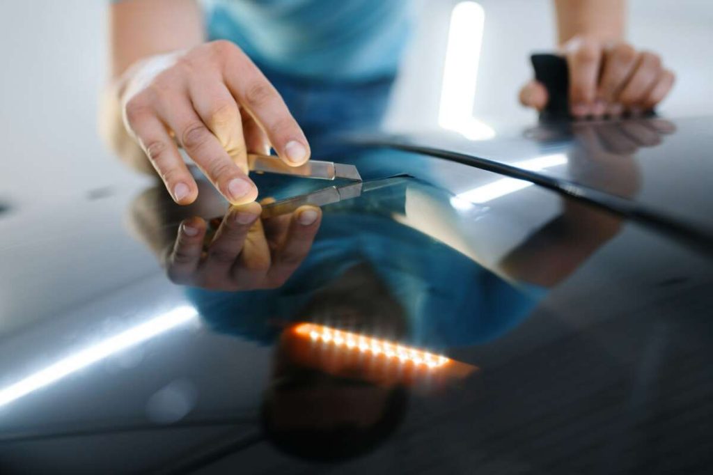 Hands skillfully use a tool to repair a dent on a car's surface, an essential step before applying paint protection film, as part of comprehensive training.