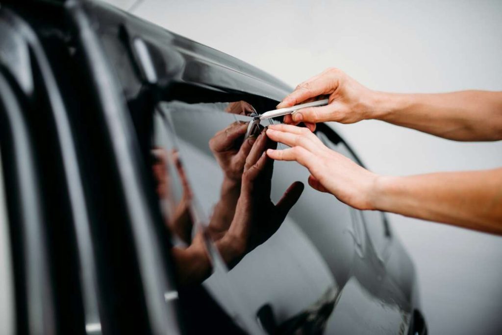 Hands expertly applying tinted film to a car window using a tool for precise fitting, showcasing techniques akin to paint protection film training.