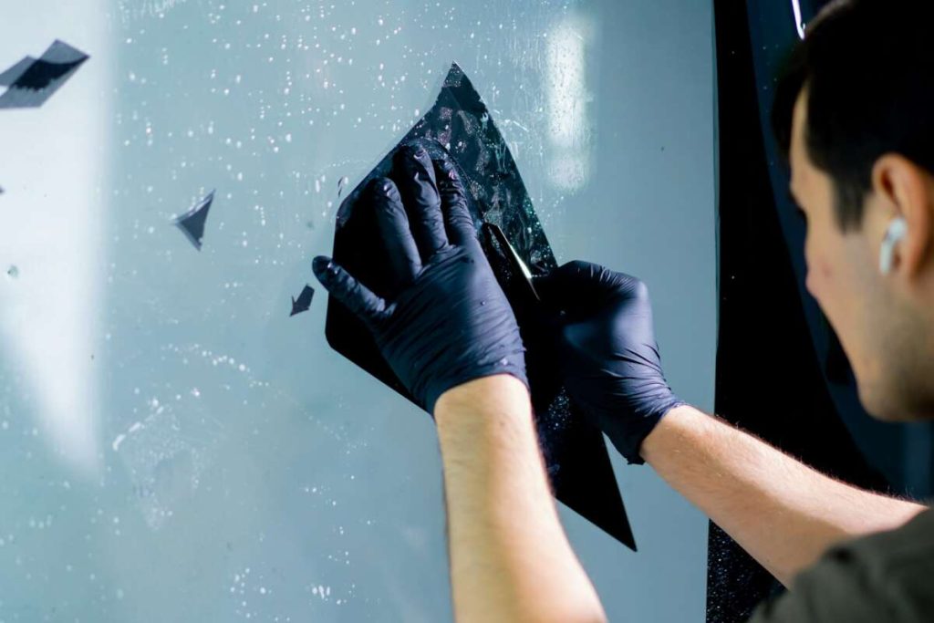 Person wearing gloves carefully applies window tint film to a glass surface, demonstrating precision and skill reminiscent of Paint Protection Film Training.