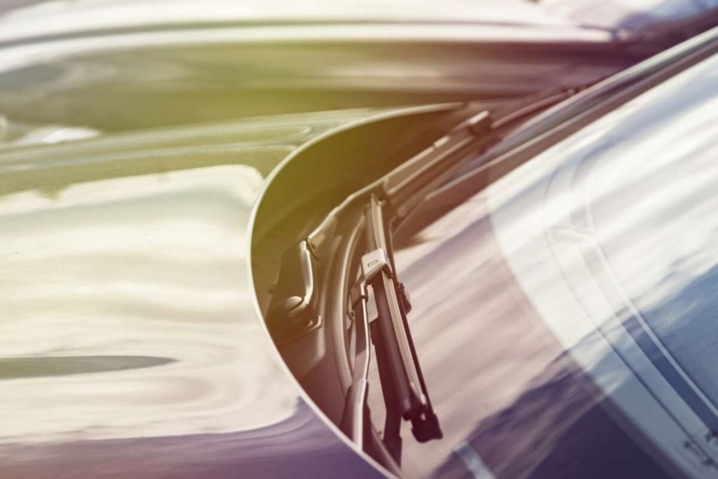 Close-up of a windshield wiper on a car, with sunlight elegantly reflecting off the windshield. The blurred background hints at motion while subtly showcasing the benefits of paint protection film training to maintain that pristine look.